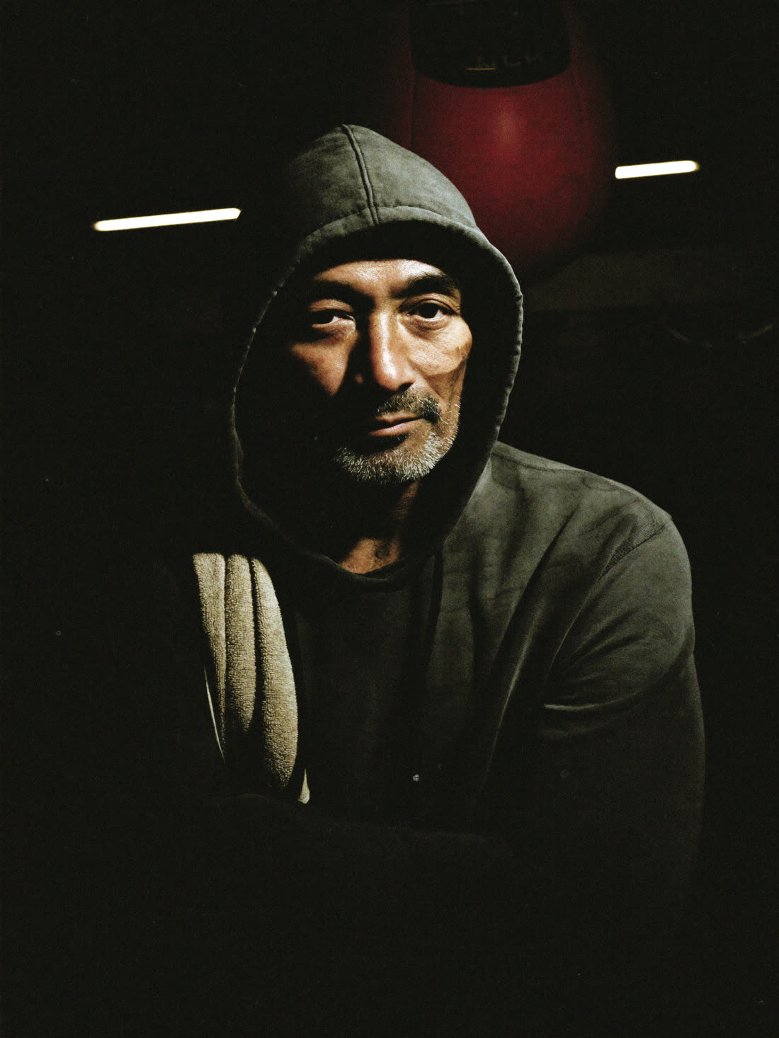 Portrait of head coach Ray Delgado in harsh gym light, arms crossed